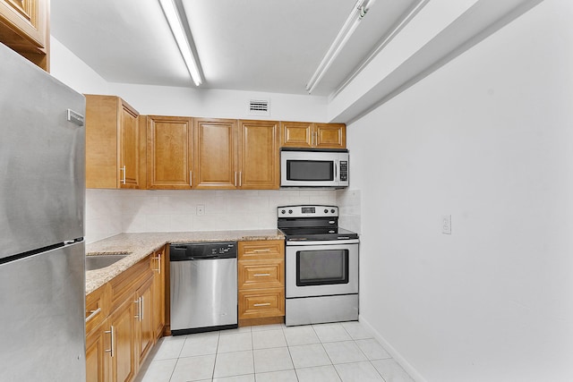 kitchen with tasteful backsplash, sink, light tile patterned floors, light stone counters, and stainless steel appliances