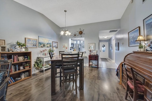 dining space with visible vents, baseboards, a chandelier, lofted ceiling, and wood finished floors