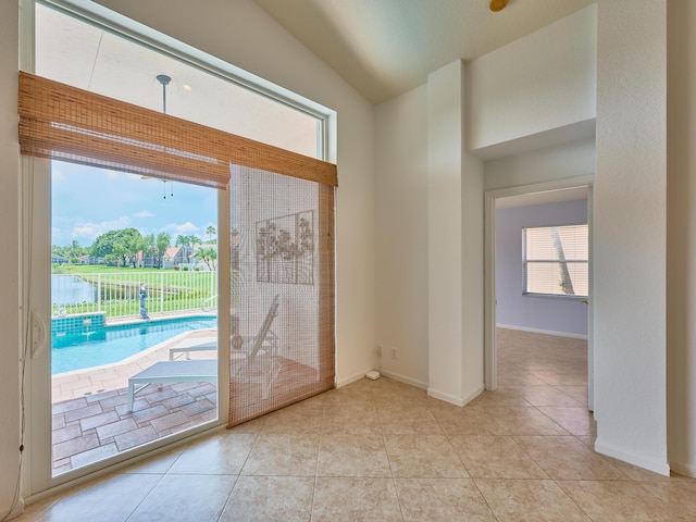 doorway with light tile patterned floors, vaulted ceiling, and a water view