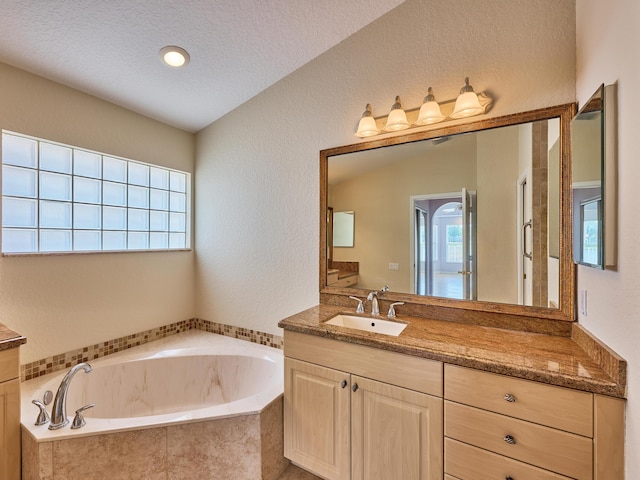 bathroom with vanity, tiled tub, and a textured ceiling