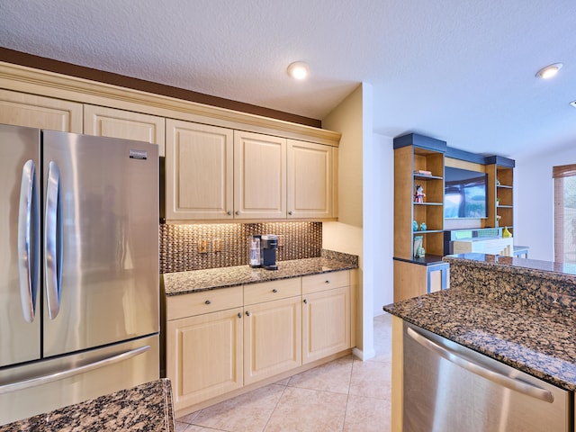 kitchen featuring appliances with stainless steel finishes, dark stone countertops, backsplash, a textured ceiling, and light tile patterned flooring