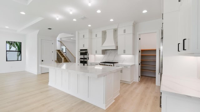 kitchen with custom exhaust hood, light stone countertops, white cabinets, and a large island with sink