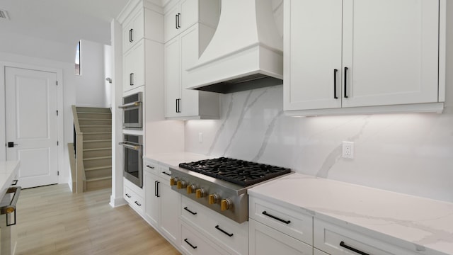 kitchen with light stone counters, custom exhaust hood, stainless steel appliances, and white cabinets