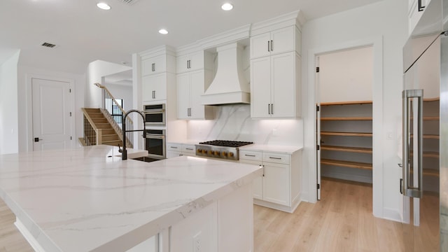 kitchen featuring sink, custom exhaust hood, light stone counters, stainless steel appliances, and white cabinets