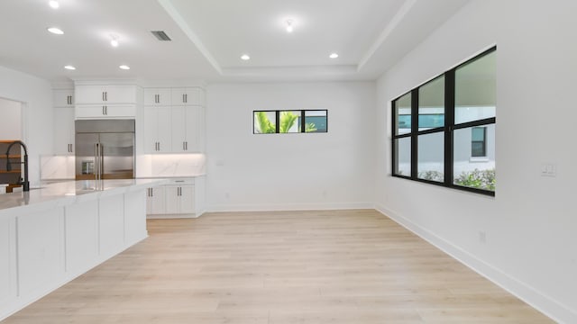 kitchen with light stone counters, white cabinets, light hardwood / wood-style flooring, and stainless steel built in fridge