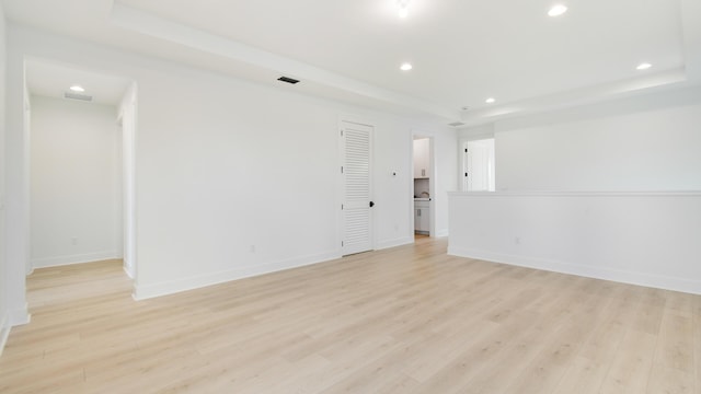 empty room with light hardwood / wood-style floors and a tray ceiling