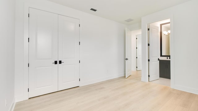 unfurnished bedroom featuring connected bathroom, light wood-type flooring, and a closet