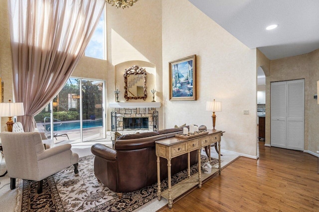 living room with a stone fireplace, a towering ceiling, and hardwood / wood-style floors