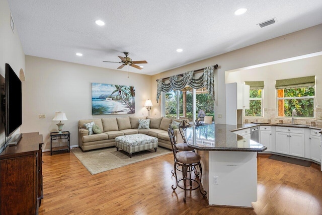 kitchen featuring sink, white cabinetry, light hardwood / wood-style flooring, a kitchen breakfast bar, and dark stone counters