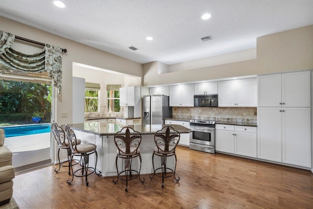 kitchen with stainless steel appliances, a kitchen island, white cabinets, and a kitchen bar