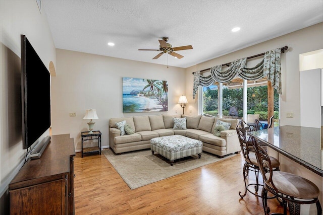 living room with a textured ceiling, ceiling fan, and light hardwood / wood-style flooring