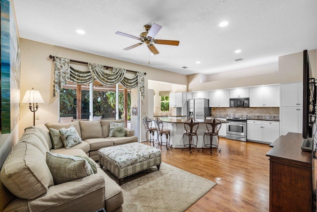 living room featuring ceiling fan, a textured ceiling, and light hardwood / wood-style floors