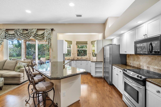 kitchen featuring white cabinetry, stainless steel appliances, a breakfast bar, and dark stone countertops