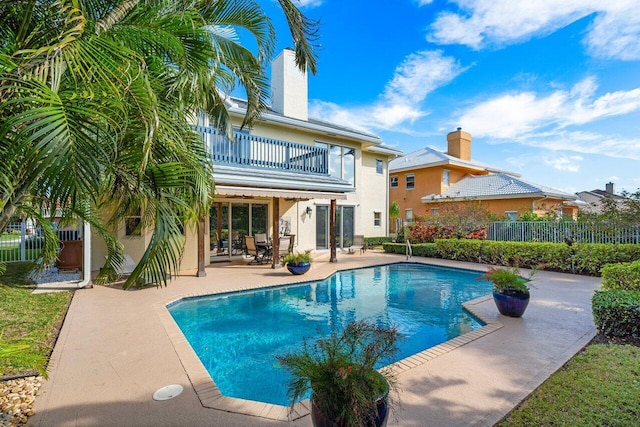 rear view of house with a fenced in pool, a patio, and a balcony