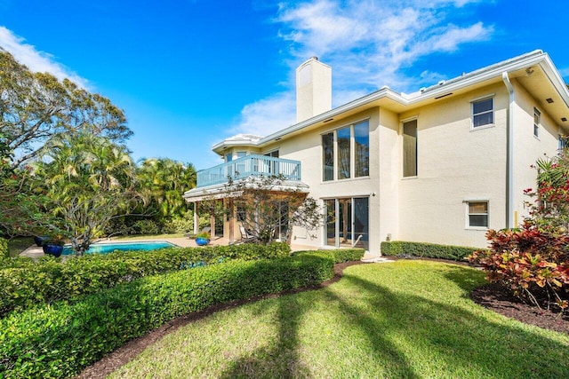 rear view of house featuring a balcony and a lawn