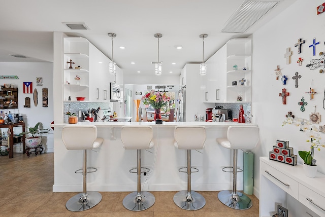 kitchen with pendant lighting, a kitchen bar, stainless steel appliances, and white cabinets