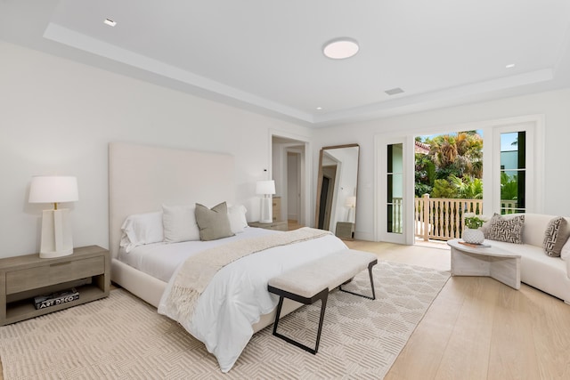 bedroom with access to exterior, a raised ceiling, and light hardwood / wood-style floors