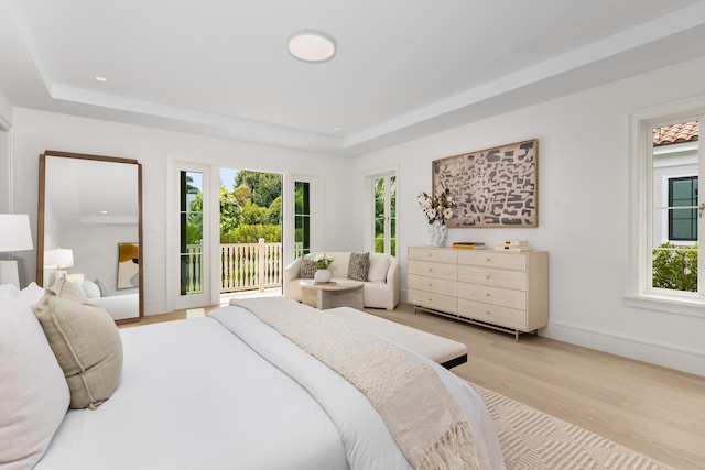 bedroom with a tray ceiling, access to outside, and light hardwood / wood-style floors