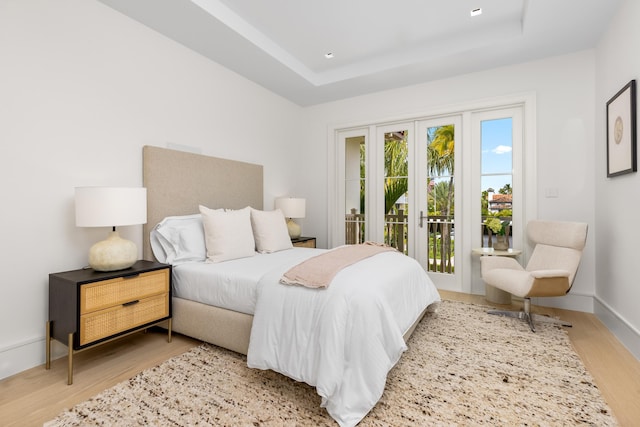 bedroom with french doors, light hardwood / wood-style flooring, access to outside, and a tray ceiling