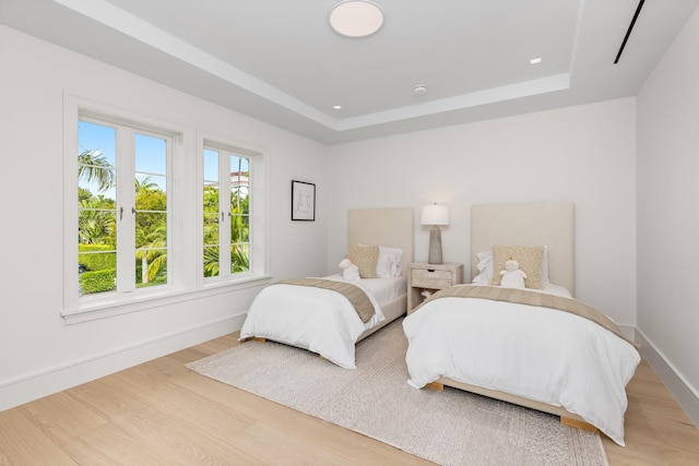 bedroom with light hardwood / wood-style floors and a raised ceiling