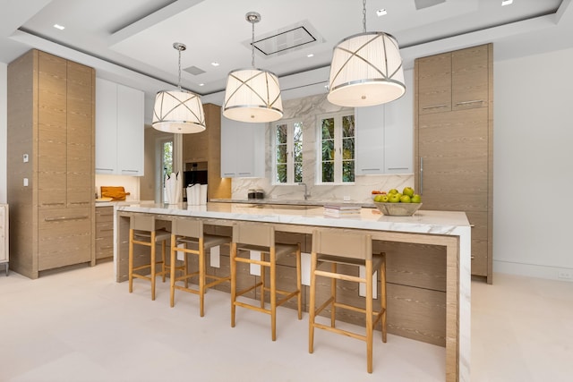 kitchen with light stone countertops, a large island, white cabinets, and decorative light fixtures