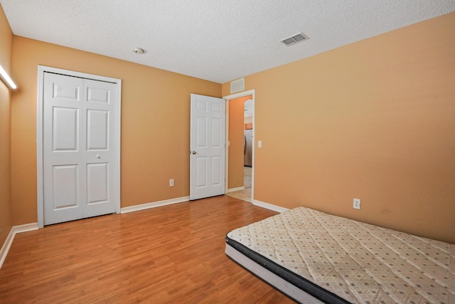 unfurnished bedroom with wood-type flooring, a closet, and a textured ceiling