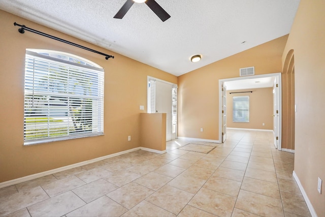 tiled empty room with ceiling fan, lofted ceiling, and a textured ceiling