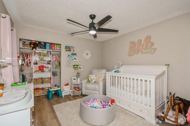 bedroom featuring a crib, ceiling fan, a textured ceiling, dark hardwood / wood-style flooring, and a closet