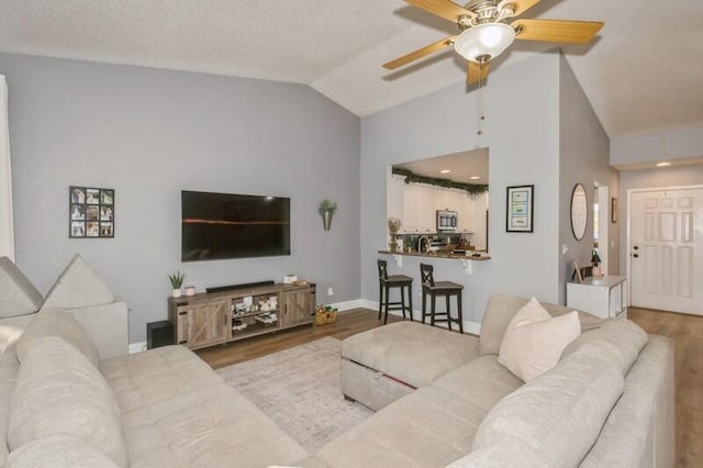 living room with ceiling fan, lofted ceiling, a textured ceiling, and light hardwood / wood-style flooring