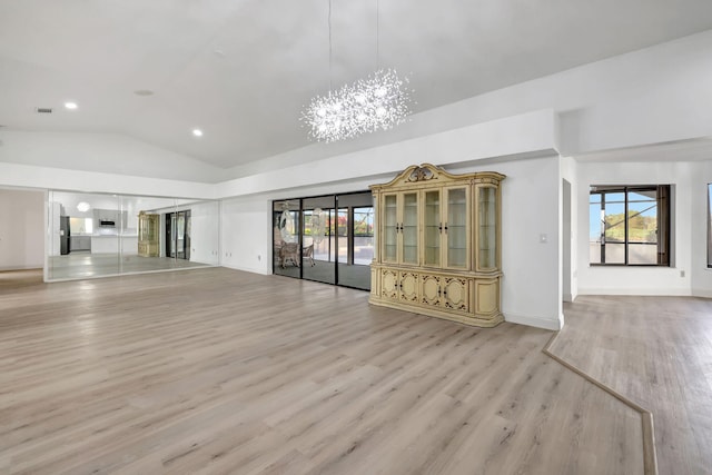 unfurnished living room with plenty of natural light, an inviting chandelier, lofted ceiling, and light hardwood / wood-style floors