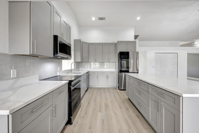 kitchen featuring sink, tasteful backsplash, light hardwood / wood-style flooring, appliances with stainless steel finishes, and gray cabinets