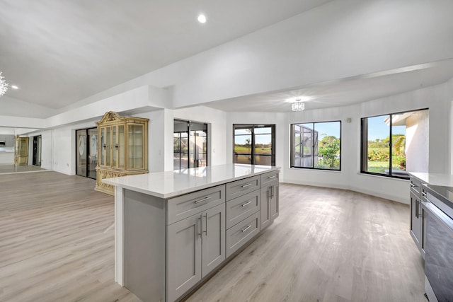 kitchen with gray cabinetry, light stone counters, a center island, vaulted ceiling, and light hardwood / wood-style floors