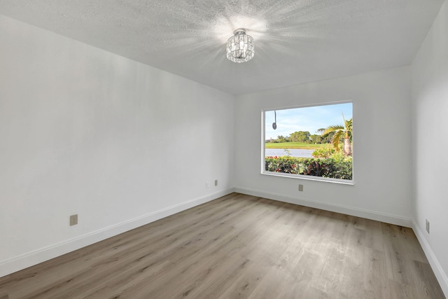 spare room featuring an inviting chandelier, a textured ceiling, and light wood-type flooring