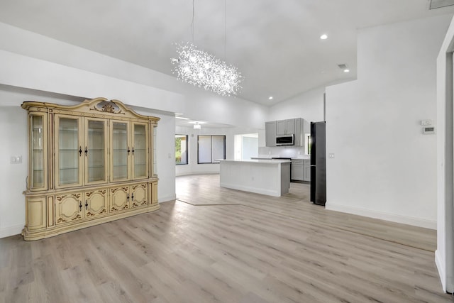 unfurnished living room with an inviting chandelier, high vaulted ceiling, and light hardwood / wood-style flooring