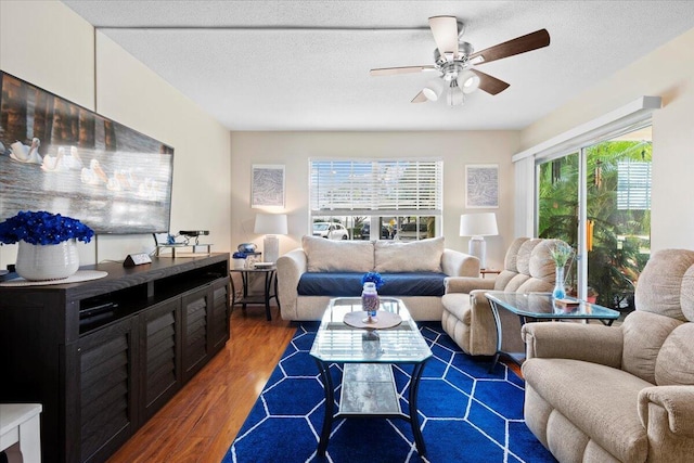 living room featuring ceiling fan, dark wood-type flooring, and a textured ceiling