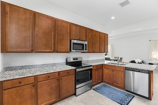 kitchen featuring appliances with stainless steel finishes, sink, light tile patterned floors, light stone counters, and kitchen peninsula