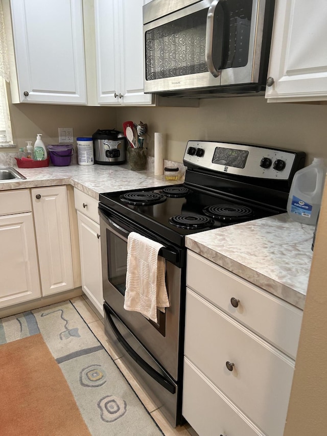 kitchen with appliances with stainless steel finishes, light tile patterned floors, and white cabinets