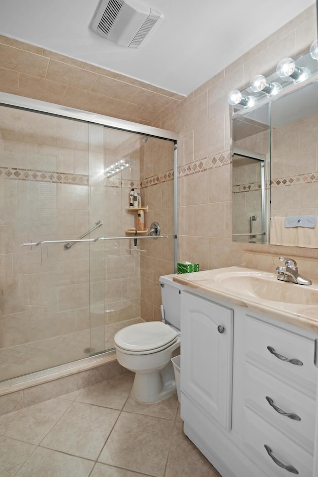 bathroom with toilet, tile walls, vanity, a shower with door, and tile patterned flooring