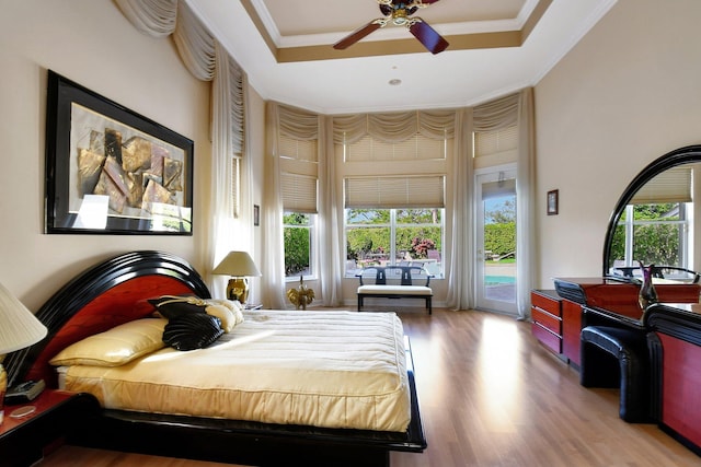 bedroom featuring crown molding, hardwood / wood-style flooring, a high ceiling, access to outside, and a raised ceiling