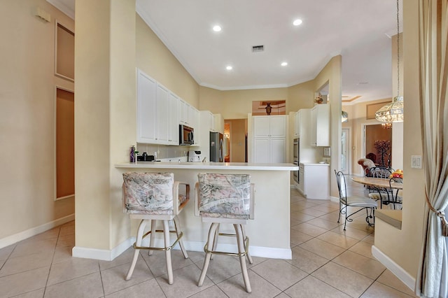 kitchen with a kitchen bar, light tile patterned floors, kitchen peninsula, stainless steel appliances, and white cabinets