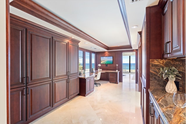 kitchen featuring a wealth of natural light, built in desk, crown molding, and dark stone counters