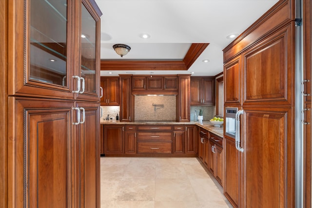 kitchen featuring ornamental molding, a tray ceiling, light stone countertops, and decorative backsplash