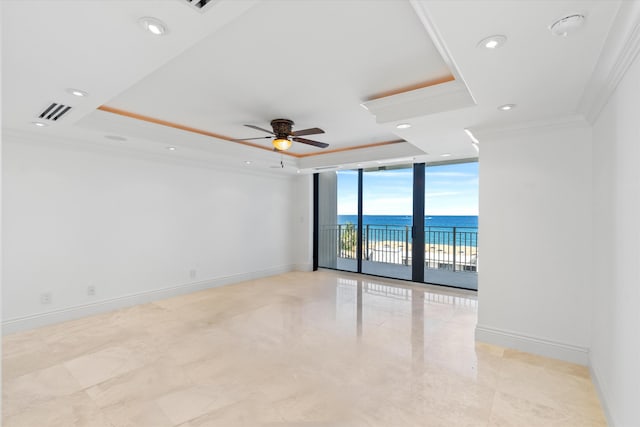 unfurnished room with a wall of windows, ceiling fan, a tray ceiling, crown molding, and a water view