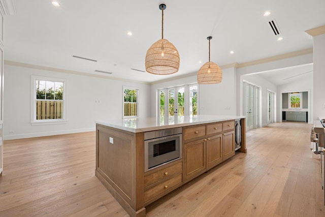 kitchen featuring a center island, brown cabinets, light wood finished floors, open floor plan, and a healthy amount of sunlight