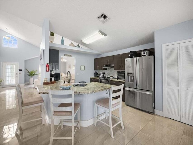 kitchen with sink, backsplash, stainless steel appliances, dark brown cabinetry, and a kitchen bar