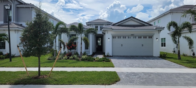 view of front of property with a garage, a front lawn, decorative driveway, and stucco siding