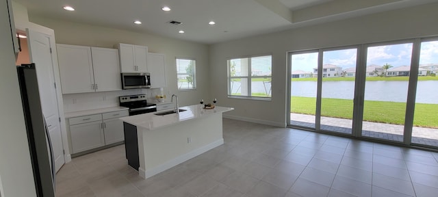 kitchen featuring stainless steel appliances, light countertops, a water view, a kitchen island with sink, and a sink