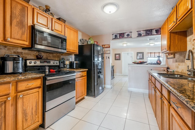 kitchen with sink, dark stone countertops, decorative backsplash, light tile patterned floors, and stainless steel appliances