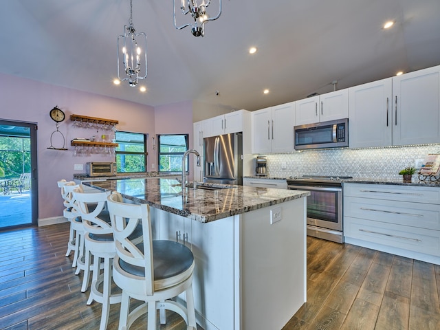 kitchen with decorative light fixtures, white cabinetry, an island with sink, a kitchen breakfast bar, and stainless steel appliances