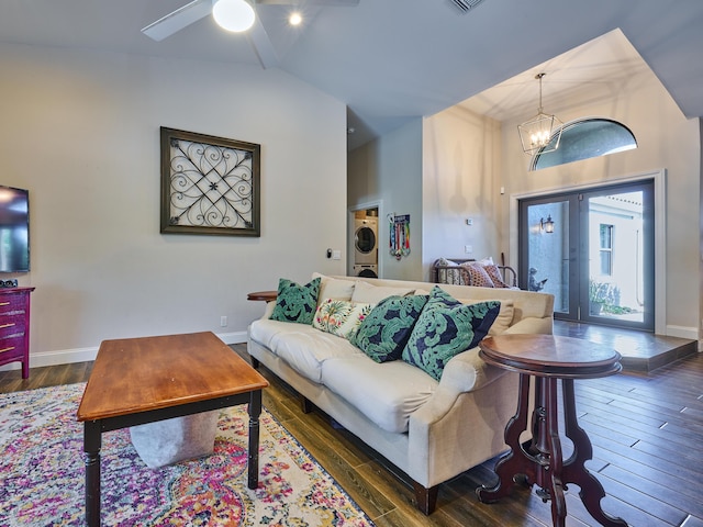 living room with french doors, lofted ceiling, dark hardwood / wood-style floors, stacked washer / dryer, and ceiling fan with notable chandelier